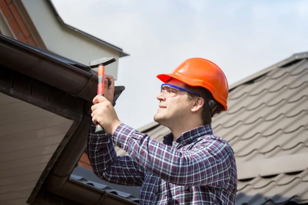 Our-Gutter-Installation-Services Young handyman working on gutter installation with hammer.