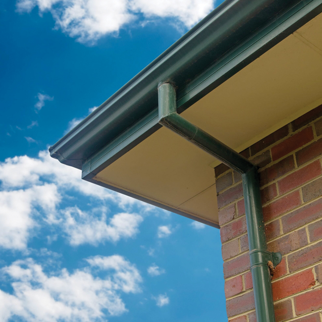 Close-up of a house gutter system on a brick wall under a blue sky, representing well-maintained gutter repair.