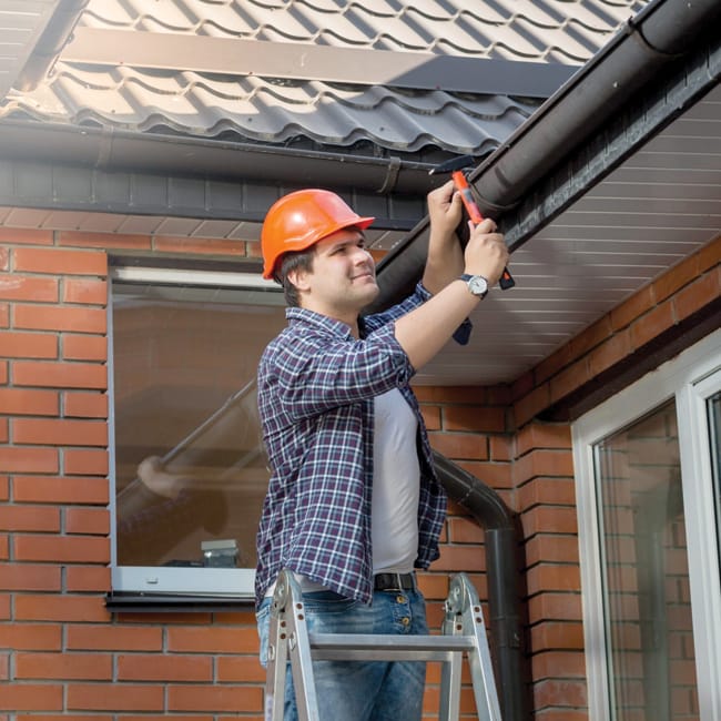 Worker standing on step ladder and repairing gutter on house