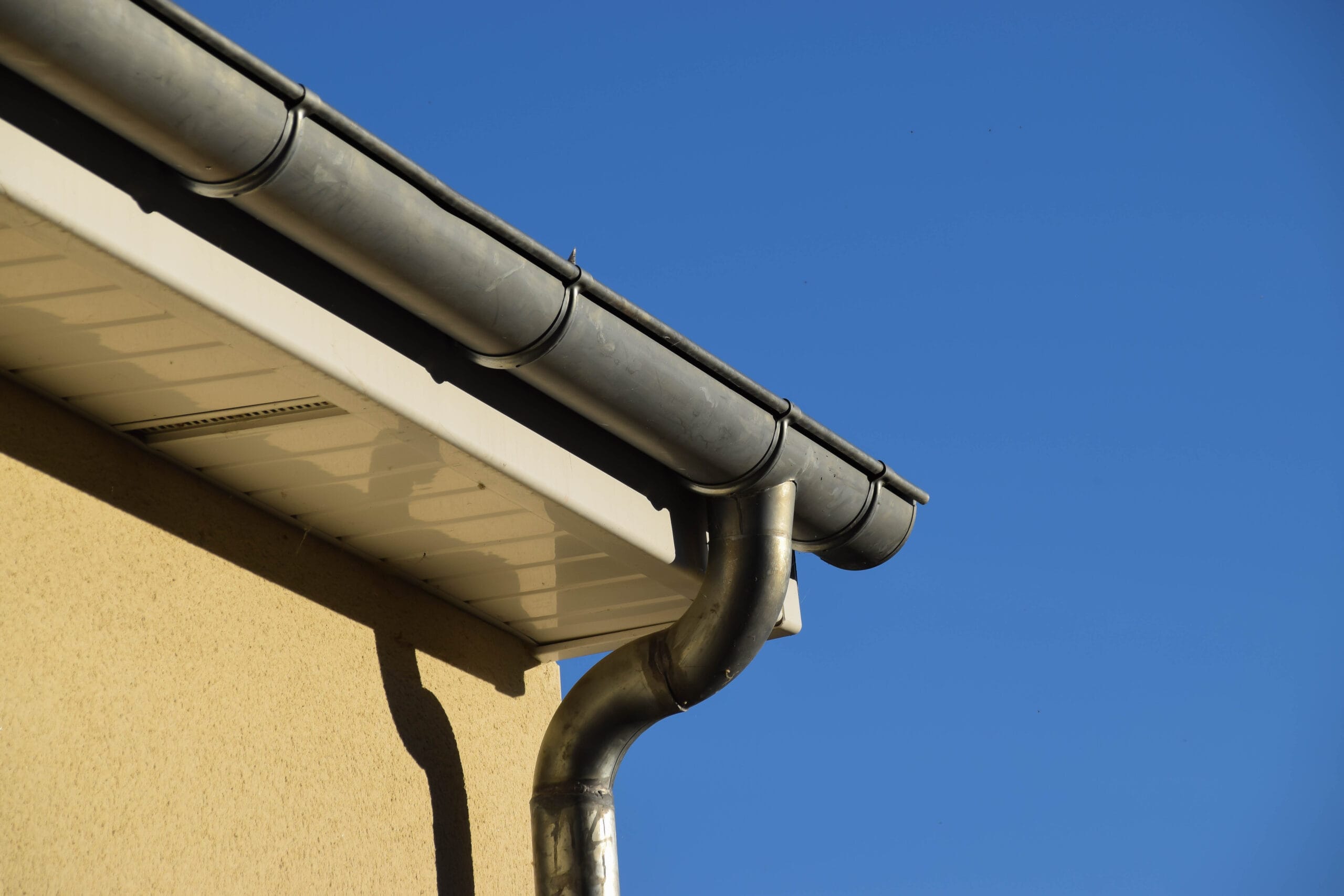 gutter-roof-install-with-clear-blue-sky-backgroud Metal gutter system on a house after gutter installation.