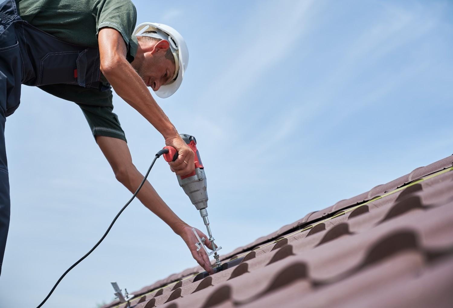 Worker performing residential metal roof repair with power drill